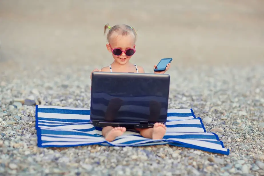 Kleines Mädchen mit Laptop und Handy am Strand.