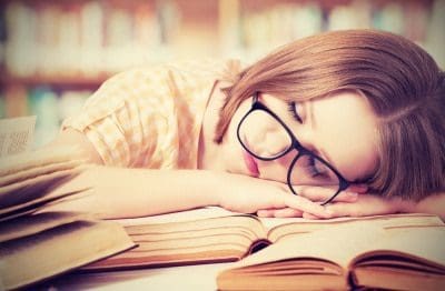 Frau schläft über Büchern ein.