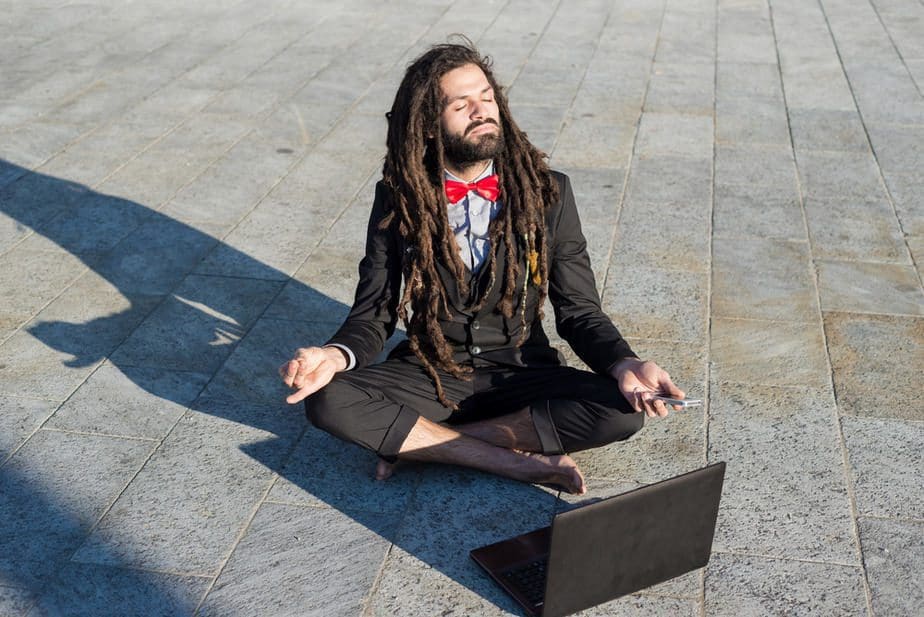 Mann mit Dreadlocks meditiert vor Laptop.