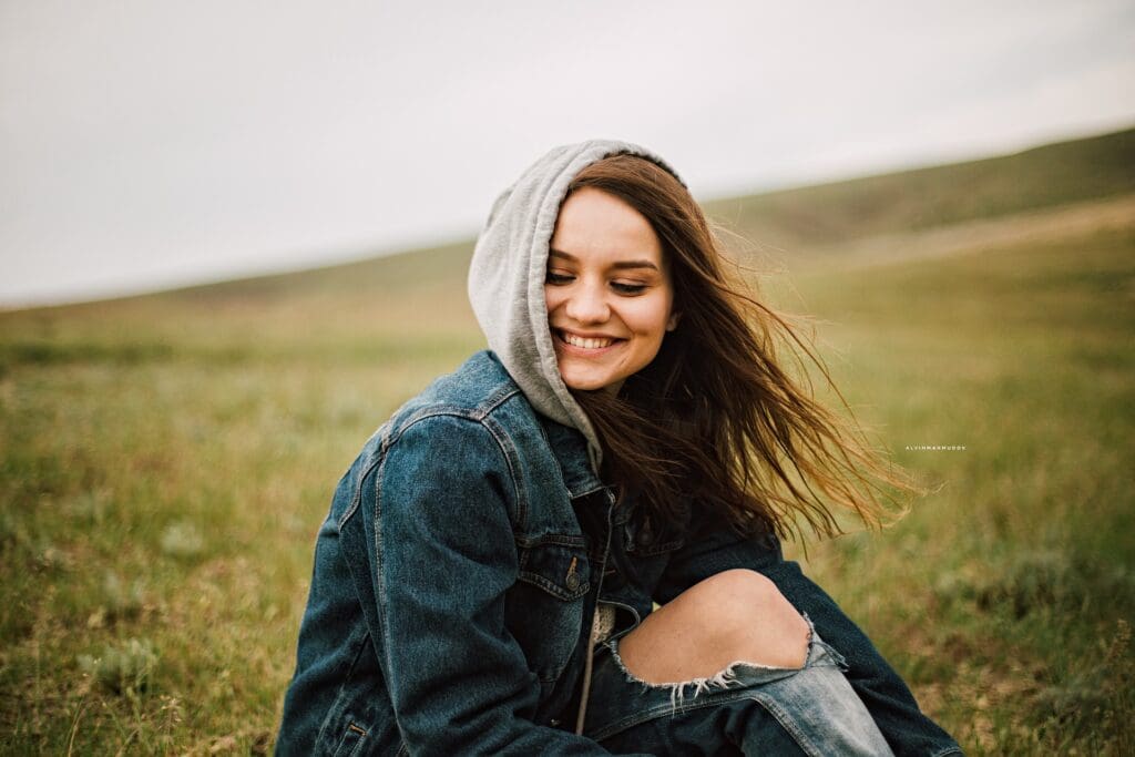 Lächelnde Frau mit Kapuze und Jeansjacke im Gras.